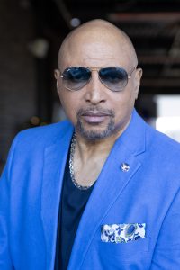 elegant middle black male in a blue suit and navy blue shirt wearing Rayban sunglasses