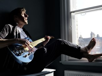 man sitting by the window playing the guitar