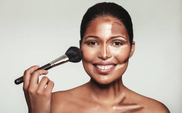 Close up portrait of contour and highlight makeup on female model. Woman applying makeup on her face with brush.