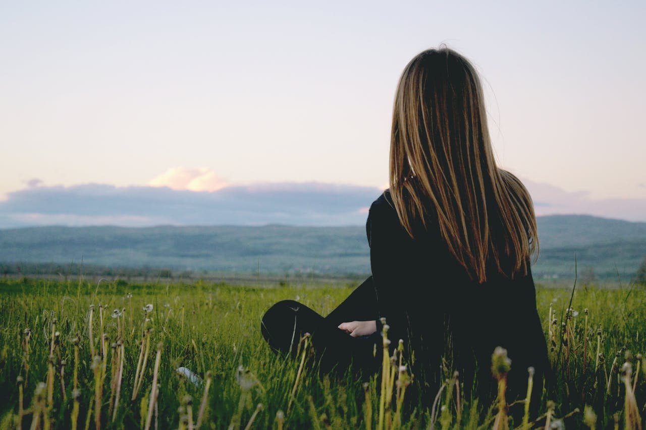 woman-wearing-black-long-sleeved-shirt-sitting-on-green-grass-field-