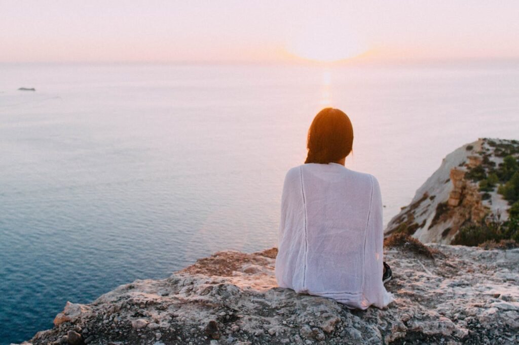 woman-sitting-on-gray-rock-near-body-of-water