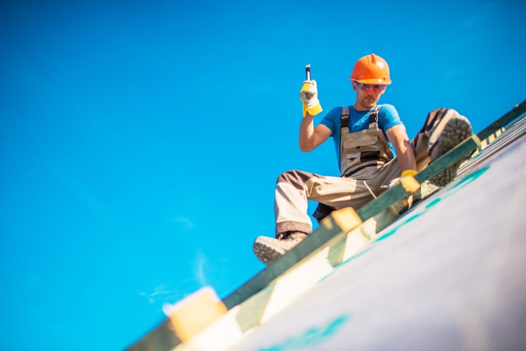 House Roof Construction Works. Caucasian Worker in His 30s on the New Building Roof. Hammer Works.
