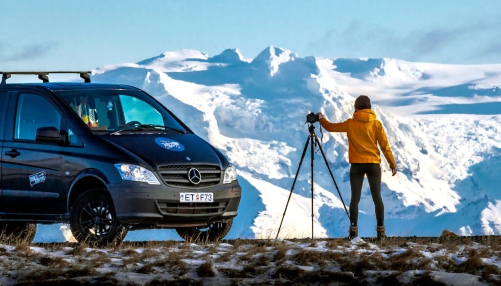 Woman photographing Iceland’s glacier landscape next to a Cozy Campers van – wellness road trip in Iceland