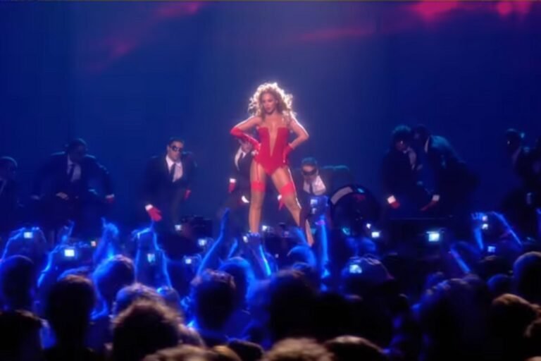 Beyoncé performing live on stage in a red outfit with dancers and a cheering crowd