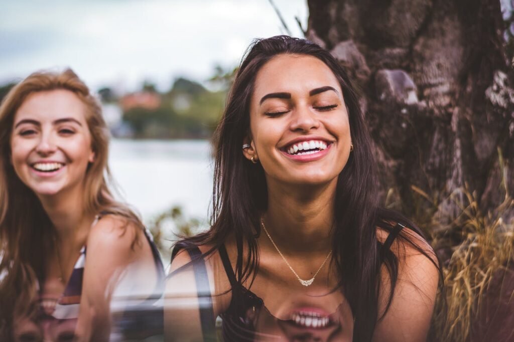 Two happy women smiling outdoors, symbolizing positivity, confidence, and letting go of negativity for success.