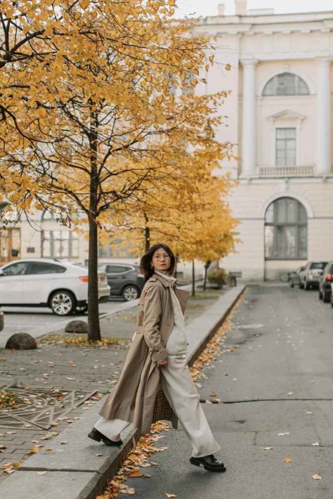 Neutral trench coat styled with denim, crossing an autumn city street.