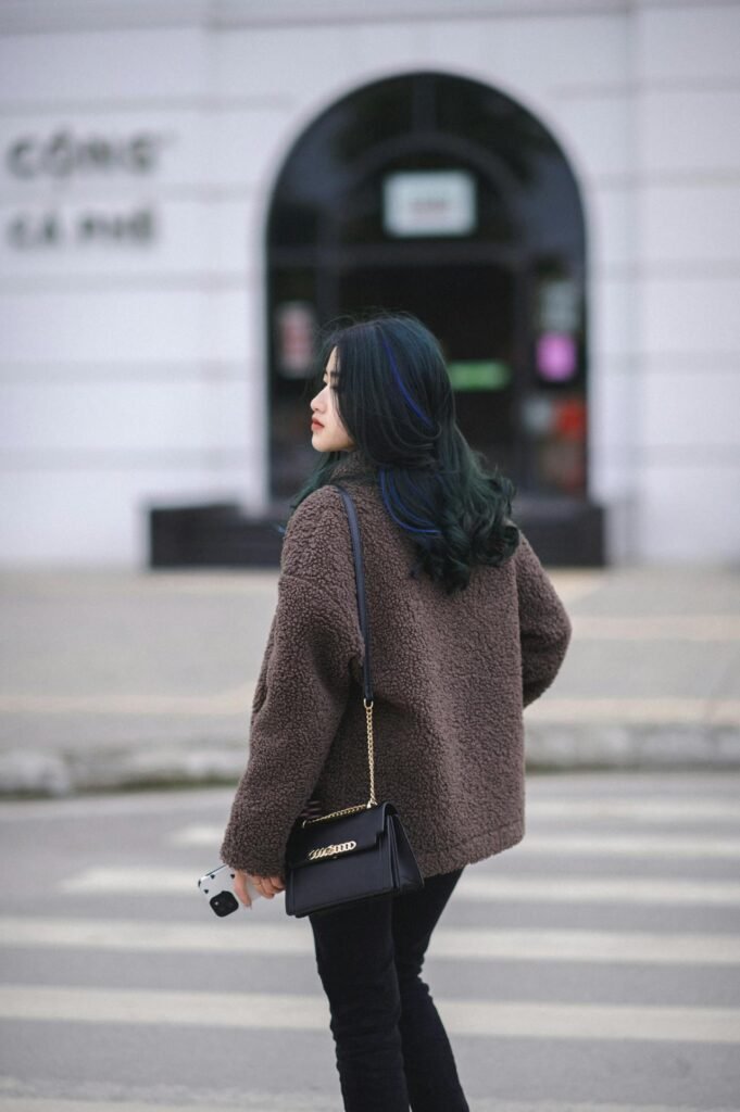 Young woman in a brown teddy coat crossing a city street.