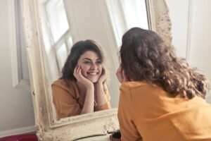 Woman smiling at herself in the mirror symbolizing confidence, clarity, and overcoming anxiety.