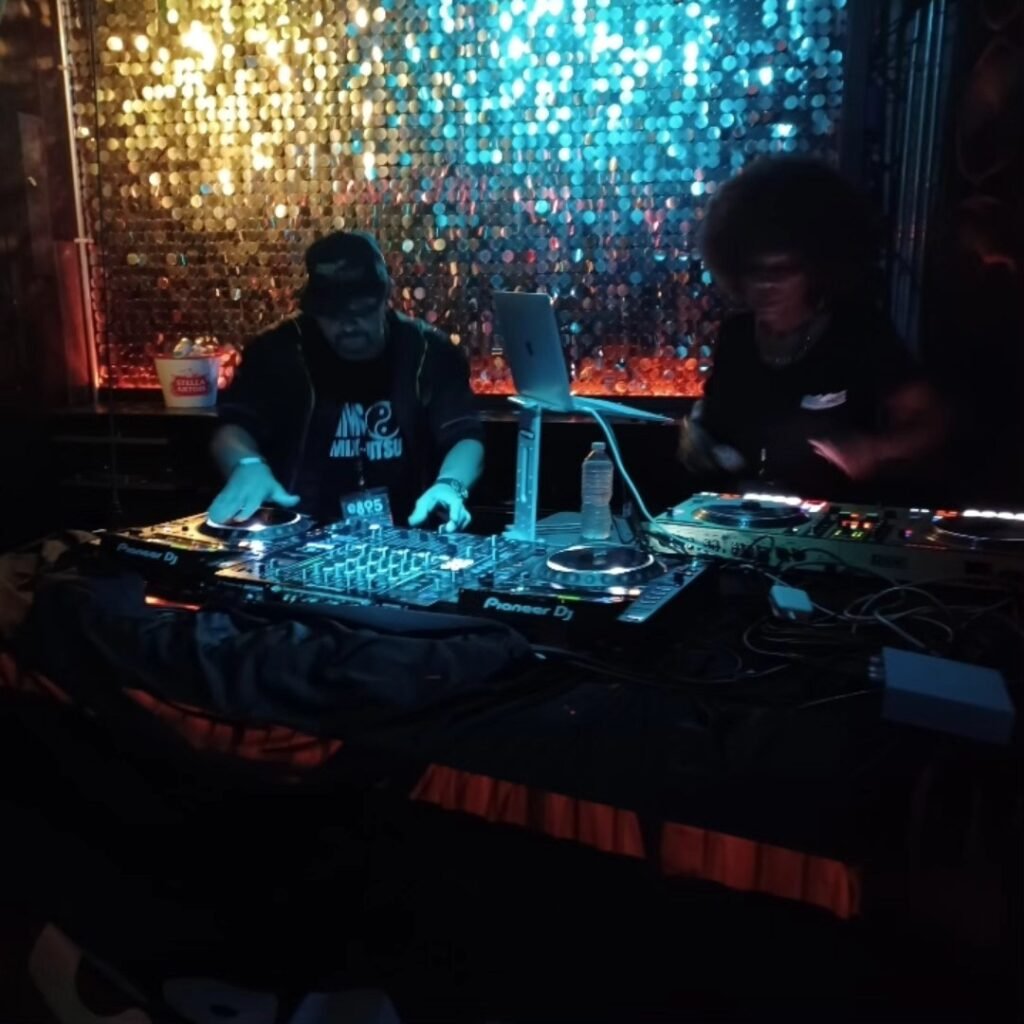 GrandMixer GMS and DJ Lady Love performing together on a Pioneer DJ setup under colorful stage lighting.