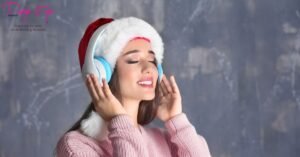 Beautiful woman wearing Santa hat and headphones smiling while listening to Christmas music – Best Christmas Songs 2025 playlist banner