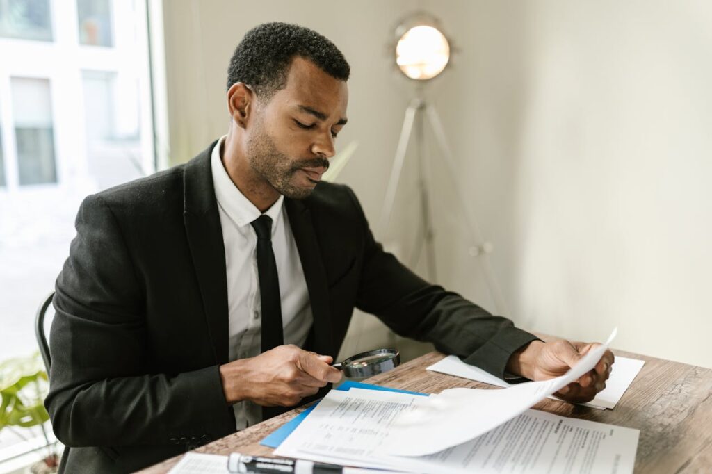 Person reviewing documents with magnifying glass.