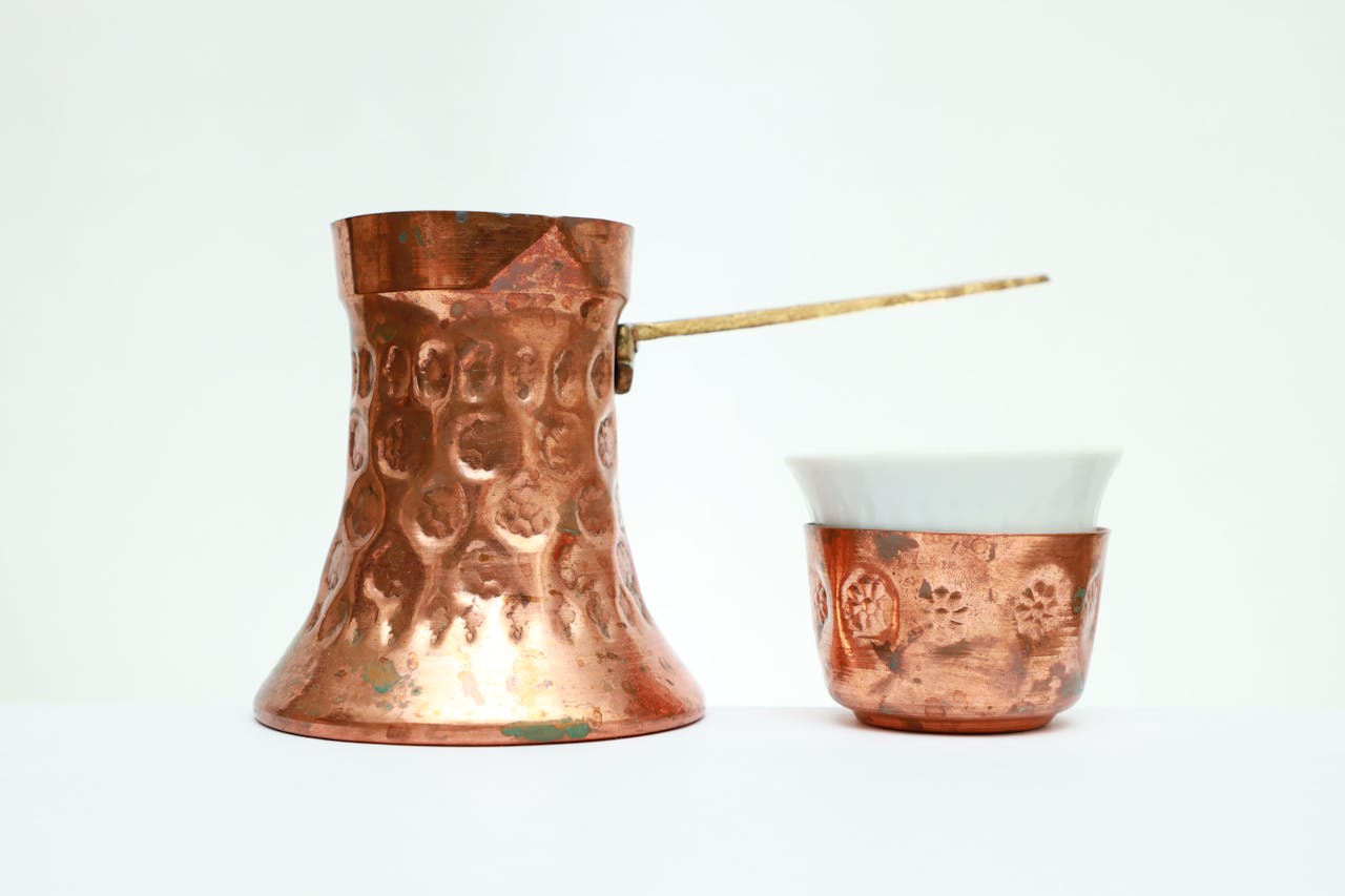 Traditional hammered copper coffee pot and cup, symbolizing ancient wellness practices and the natural antimicrobial properties of copper.