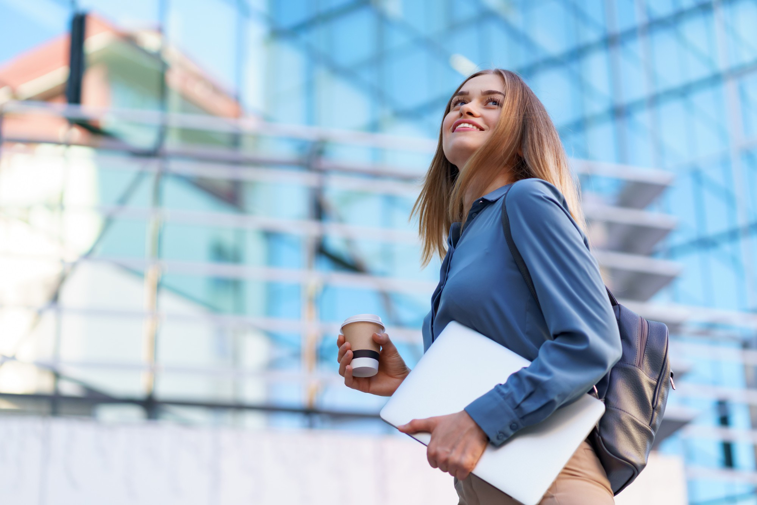 blonde-business-woman-smiling-portrait-holding-laptop-coffee-wearing-blue-gentle-shirt-modern-building-Sustainable Career