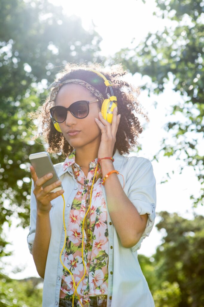 Young woman listening to a music spring reset playlist on her smartphone with wireless headphones, feeling joy and dancing in a park