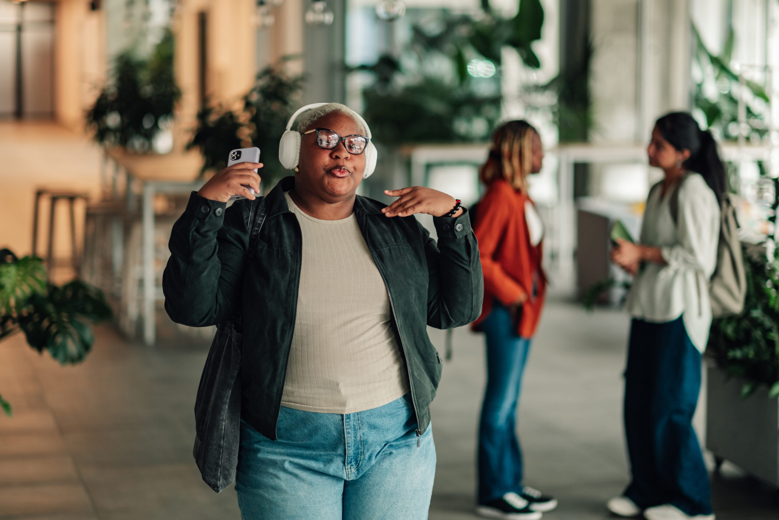 Young woman listening to a music spring playlist on her smartphone with wireless headphones, feeling joy and dancing in an office environment