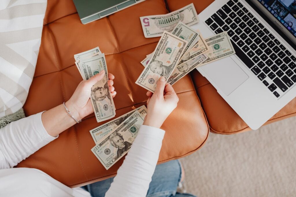 Person using a laptop while handling cash, representing AI side hustles, online income opportunities, remote work, and making extra money in 2026.