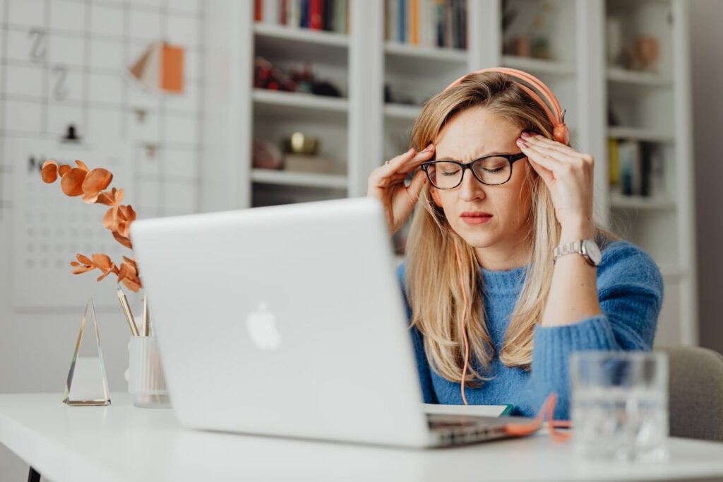 Stressed woman working on laptop representing burnout, anxiety, and habits that affect women’s confidence.