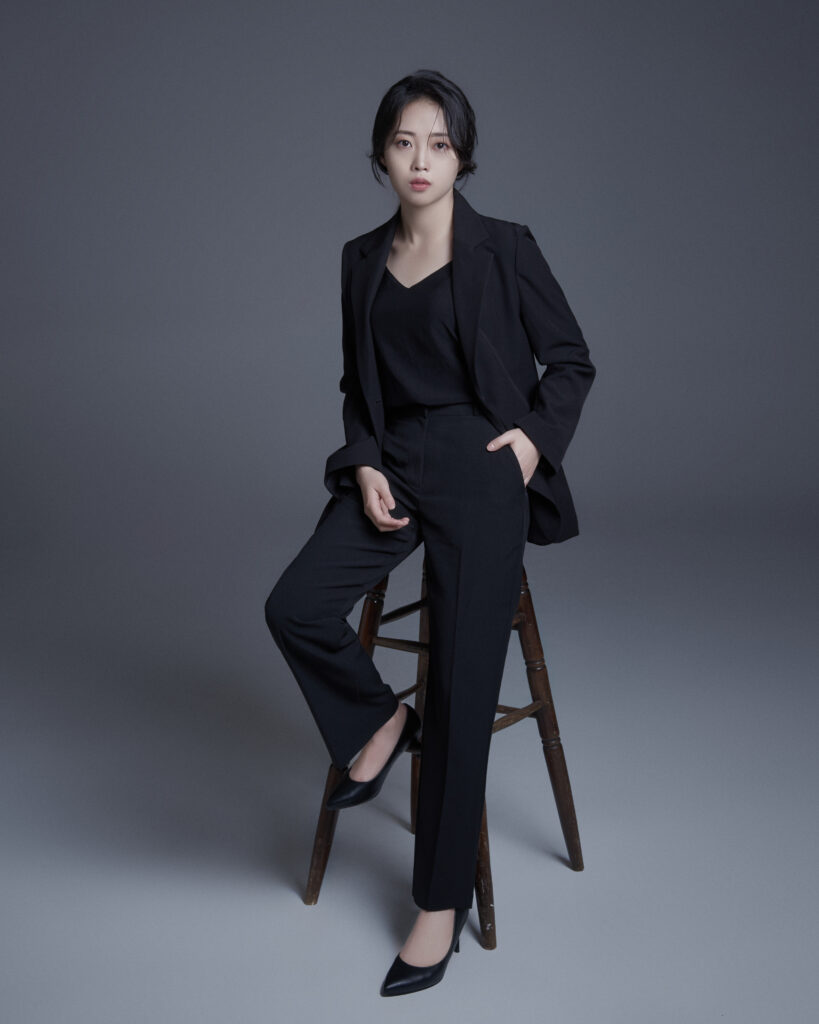Kim Sunnyeong poses in an elegant black suit during a promotional photoshoot for her debut single "Named Hyung," a Korean ballad about family, forgiveness, empathy, and emotional healing.