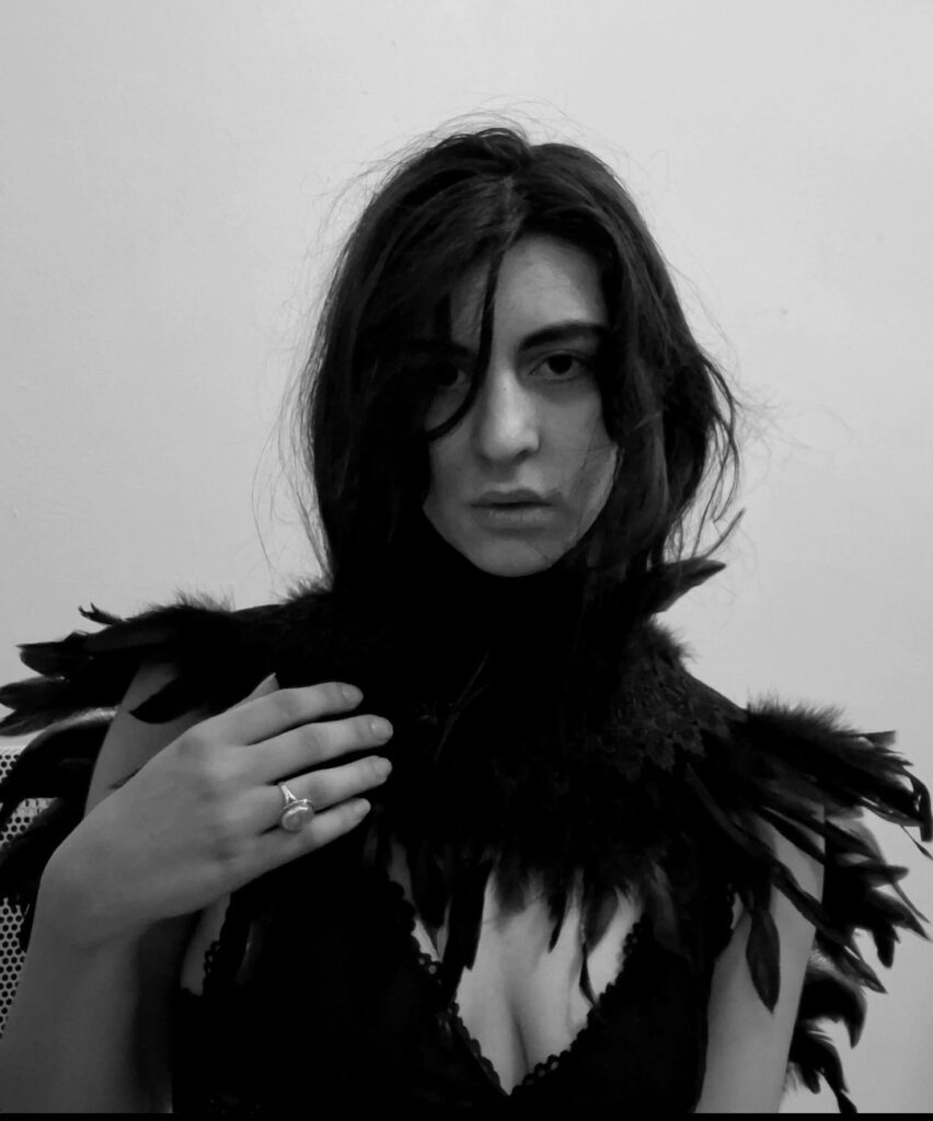 Andrea, independent alternative artist, photographed in black and white wearing dark feathered attire. Featured in a Pump It Up Magazine interview about My Polarizing Nature, artist mental health, depression, and staying true to her music.