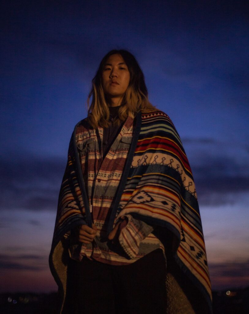 Korean artist Hanseein photographed at dusk, wearing a patterned poncho during the Bluetopink era.